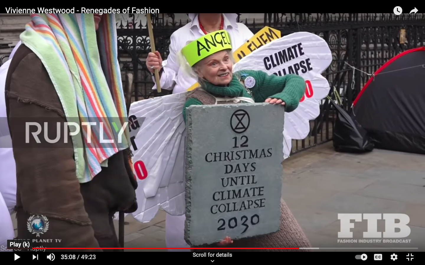 Screenshot of YouTube video still showing popular fashion designer Vivienne Westwood wearing an angel crown and holding 
        a stone-made manifesto saying Twelve Christmas Days Until Climate Collapse 2030
